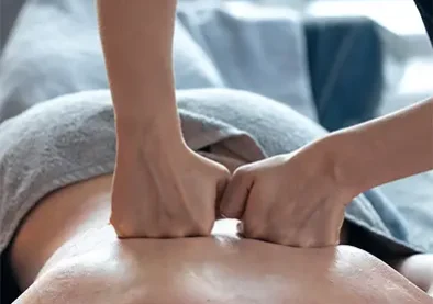 Therapist works with fists on back muscles using warm oil in a bed spa.