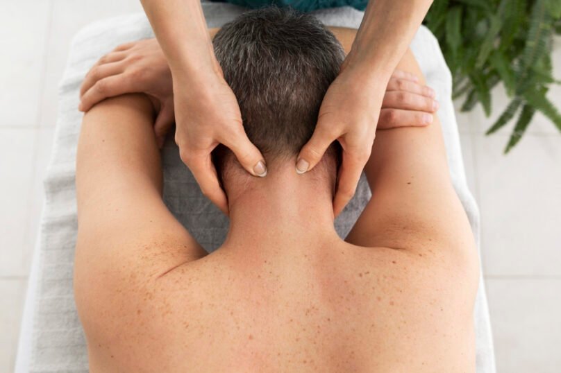 massotherapist performing neck massage at male patient